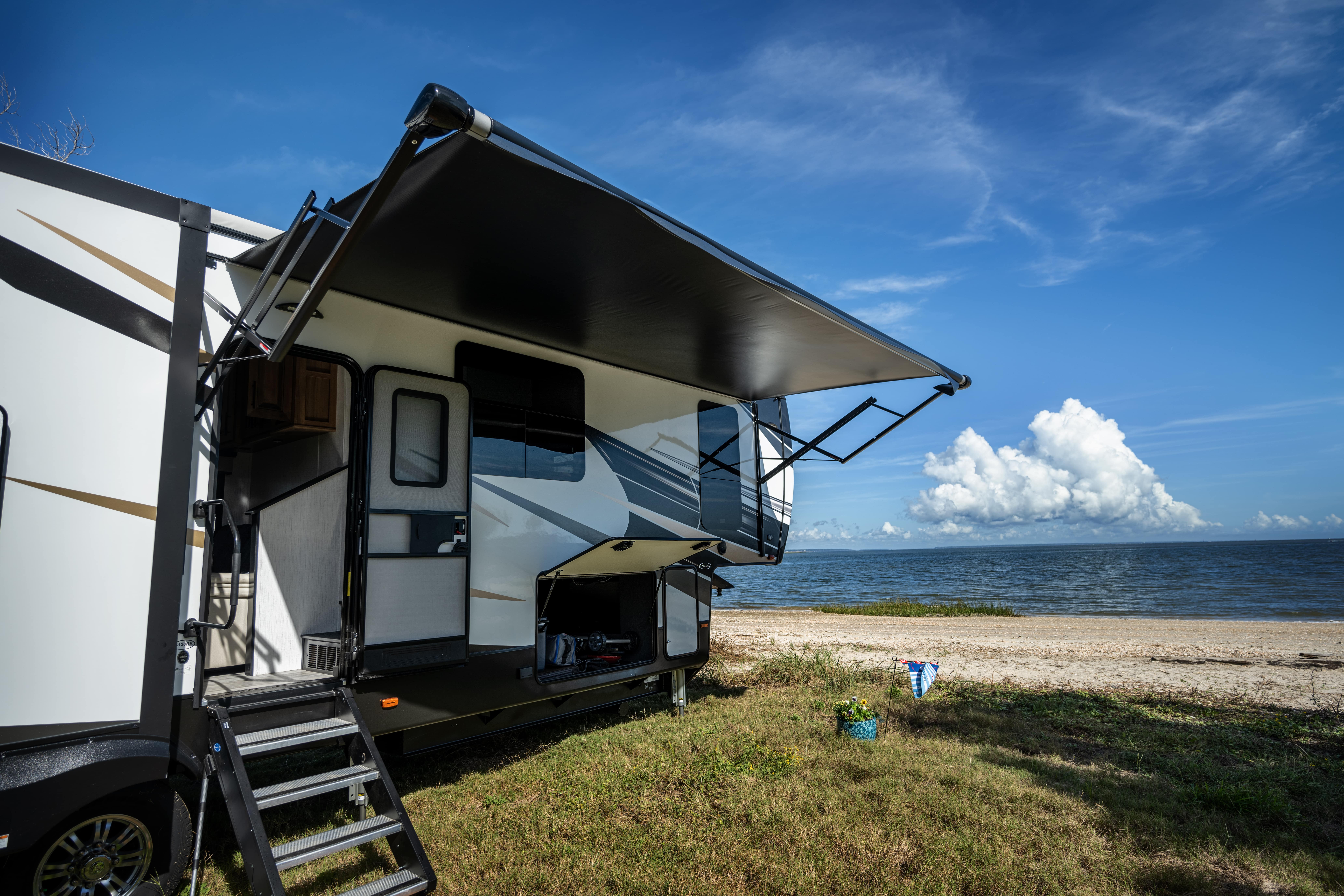 The side of an RV with an extended awning parked near the beach.