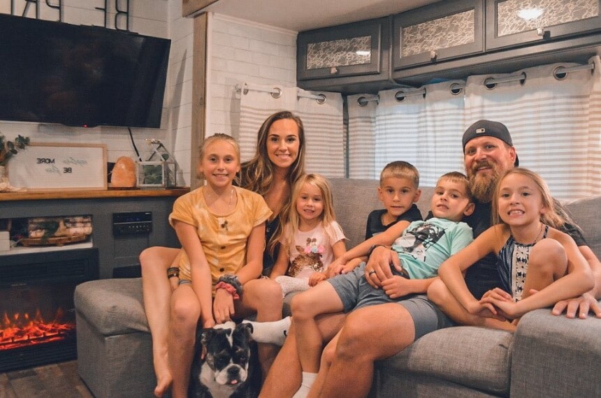 A smiling mom and dad and five kids piled together on an RV couch.