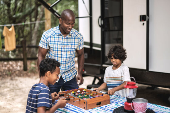A family playing games outside their RV, enjoying quality time together in a grassy area with outdoor furniture and a clear sky.