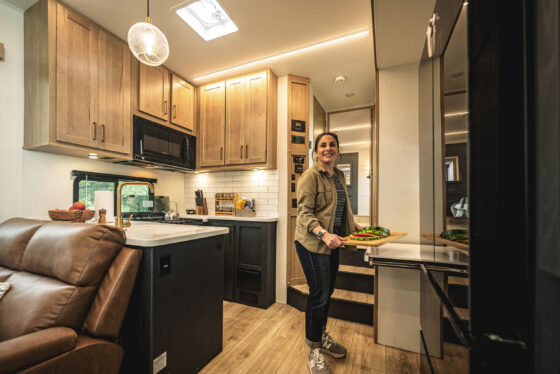 Interior view of a modern RV kitchen with a person preparing dinner on the countertop.