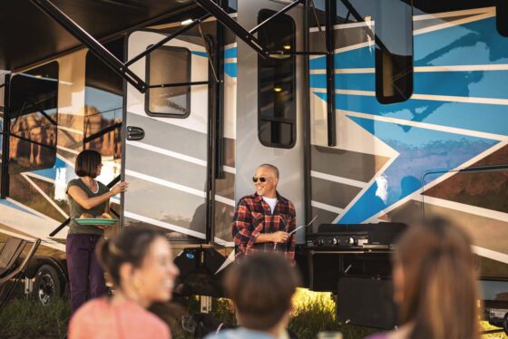 Family enjoying a cookout outside their RV, grilling food and relaxing under the awning.