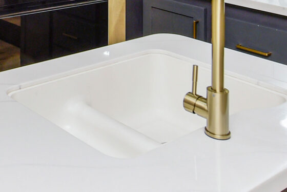 Modern sink area with clean white countertops and stylish gold faucets in an RV kitchen.