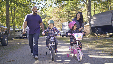Luis and Sandra walking alongside their two young kids who are riding bikes at a campground.