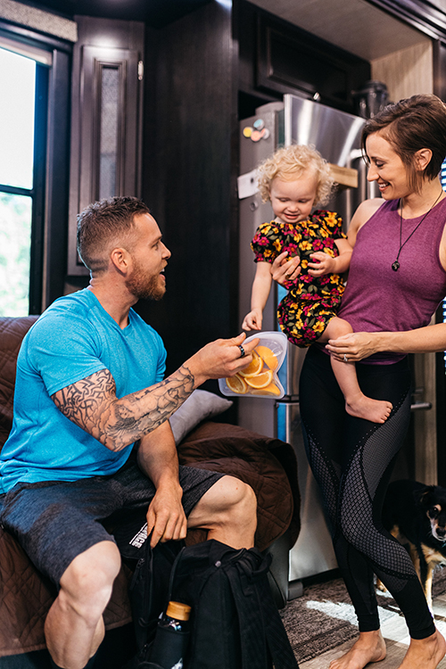 A man holding a bag of orange slices for a young child to eat.