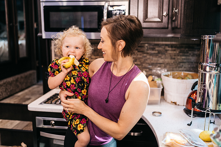 A woman holding a small child, who is smiling and eating a banana.