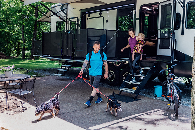 A young family leaving an RV with two dogs on a leash to go for a walk.