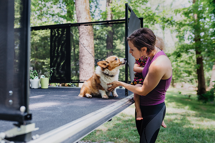 A woman petting a dog on the back of a toy hauler patio.