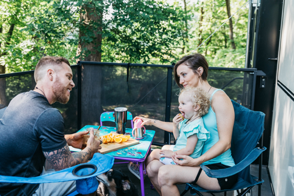 A young family eating orange slices on the back patio of an RV toy hauler.