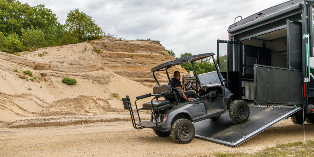 A man driving a golf cart up a toy hauler ramp.