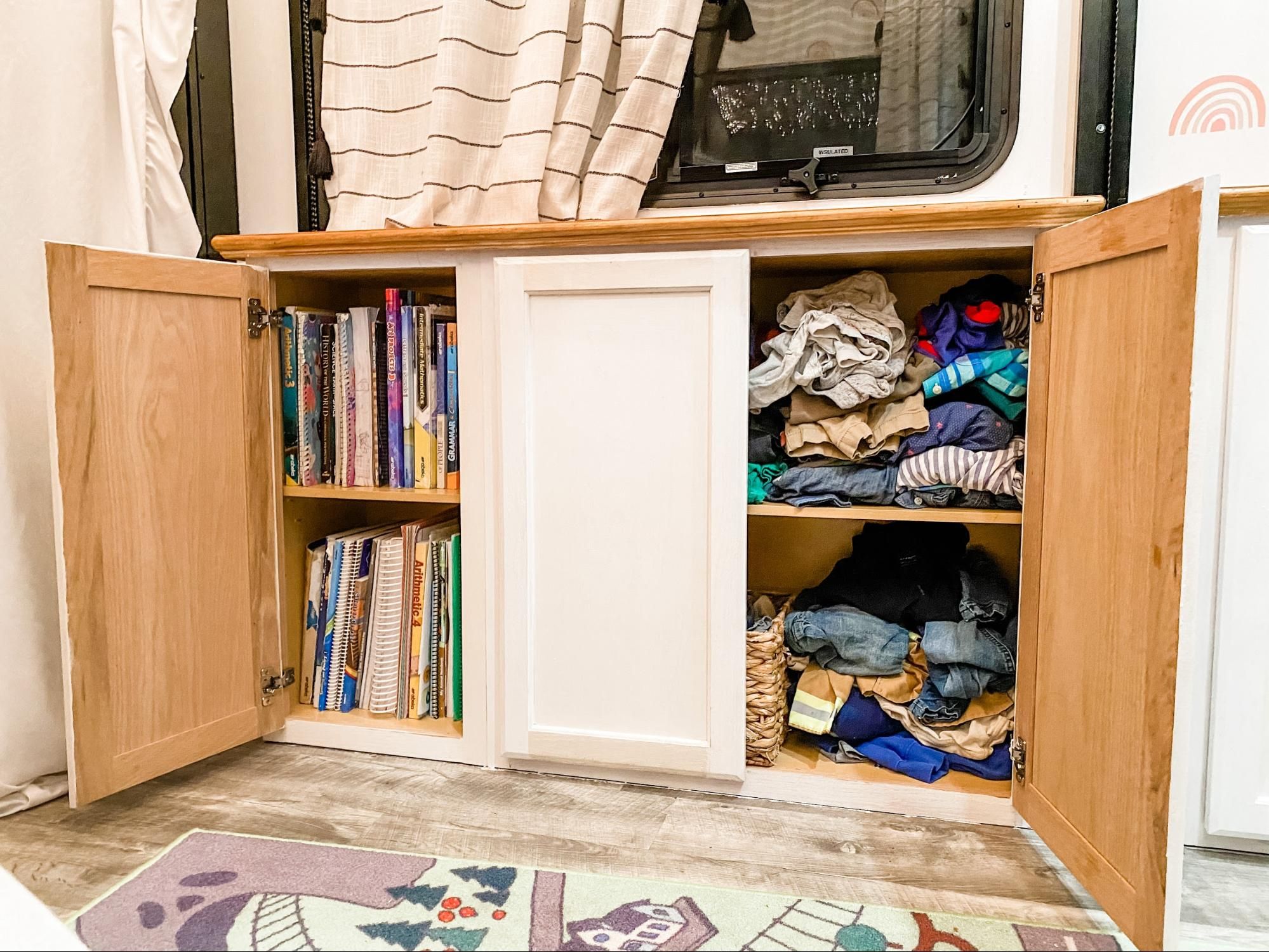 A cabinet filled with kids books and clothes.