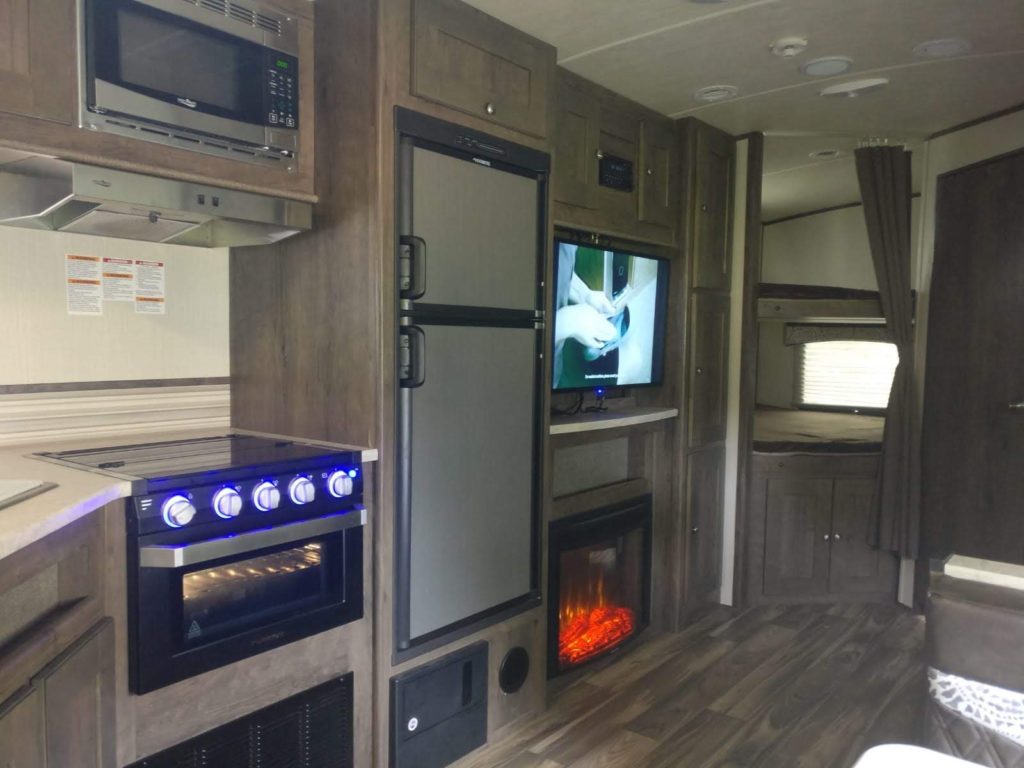 The inside of a trailer showing off a kitchen range, flat screen TV and fireplace.