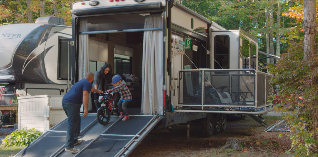 A mom and dad helping a kid walk a bike down a toy hauler ramp.