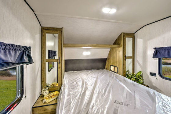 Cozy bedroom in a Pioneer travel trailer, featuring a comfortable bed and storage compartments.