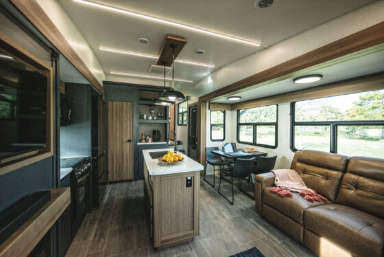 Interior view of the kitchen and living room area in the 2024 Heartland Corterra fifth-wheel RV, featuring a spacious layout with modern appliances, a comfortable seating area, and elegant finishes.