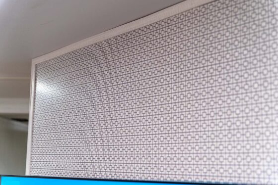 A close-up of a patterned wall panel featuring a repeating geometric design made of interlocking circles and squares in a grid, with part of a ceiling and a blue object visible at the bottom edge.