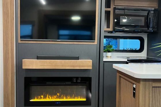Interior view of the living area in the Heartland Corterra fifth-wheel RV, featuring a modern TV and elegant fireplace beneath.