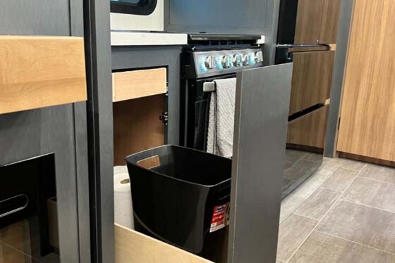 Interior view of the Heartland Corterra fifth-wheel RV kitchen, highlighting a pull-out trash can, modern appliances, and spacious cabinetry.
