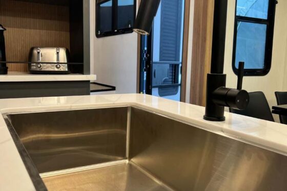 Close-up of the kitchen sink area in the Heartland Corterra fifth-wheel RV, showcasing a modern, stainless steel sink with stylish faucet and countertop.