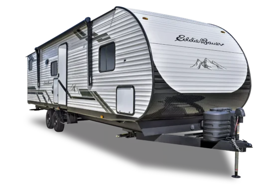 A silver and white travel trailer with Eddie Bauer branding, mountain graphic, and dual axles, featuring a side door, windows, and front hitch with propane tanks.