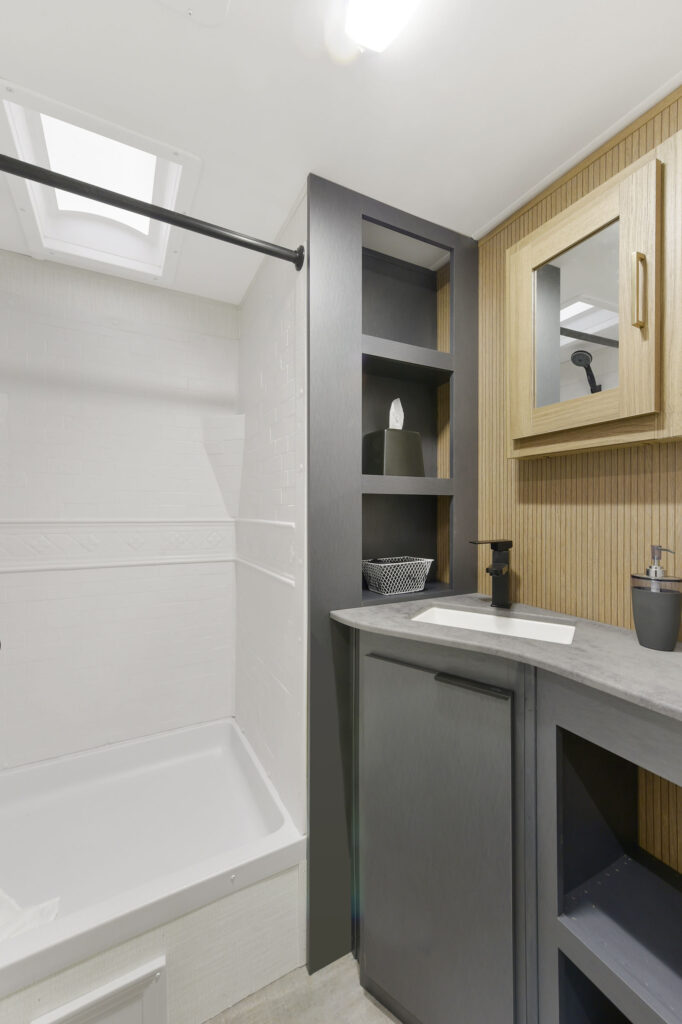 Modern bathroom with a white shower on the left, dark gray shelving and sink cabinet in the center, and a wooden medicine cabinet with a mirror on the right. The color scheme is neutral and minimalist.