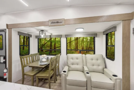 Interior of the 2024 Heartland Eddie Bauer 3100RL fifth wheel, featuring a cozy living area with theater seating, a dining table with chairs, and large windows for natural light.