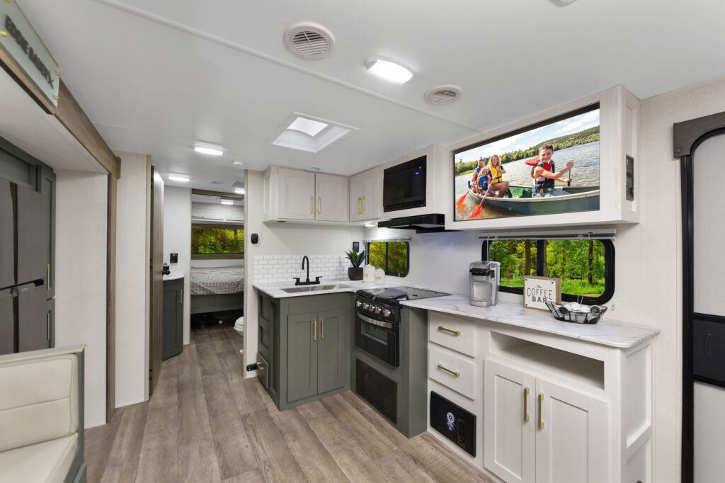 The image features the 2025 Eddie Bauer 2510RL travel trailer, showcasing its elegant and modern design. The interior highlights a spacious living area, complete with plush seating that invites relaxation and socializing. Large windows flood the space with natural light, creating an airy atmosphere. The well-appointed kitchen area includes contemporary appliances and ample counter space, perfect for preparing meals on the go. Rich wood tones and stylish accents enhance the trailer's warm and inviting ambiance. Ideal for family outings or weekend getaways, the 2510RL combines comfort and functionality, making it a great choice for outdoor adventures.