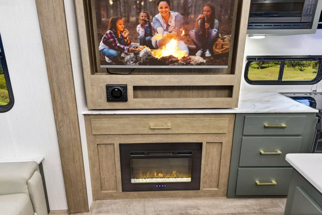 Living room area of the 2025 Eddie Bauer CWEL 3311RL RV with table under TV and marble countertop above the fireplace.
