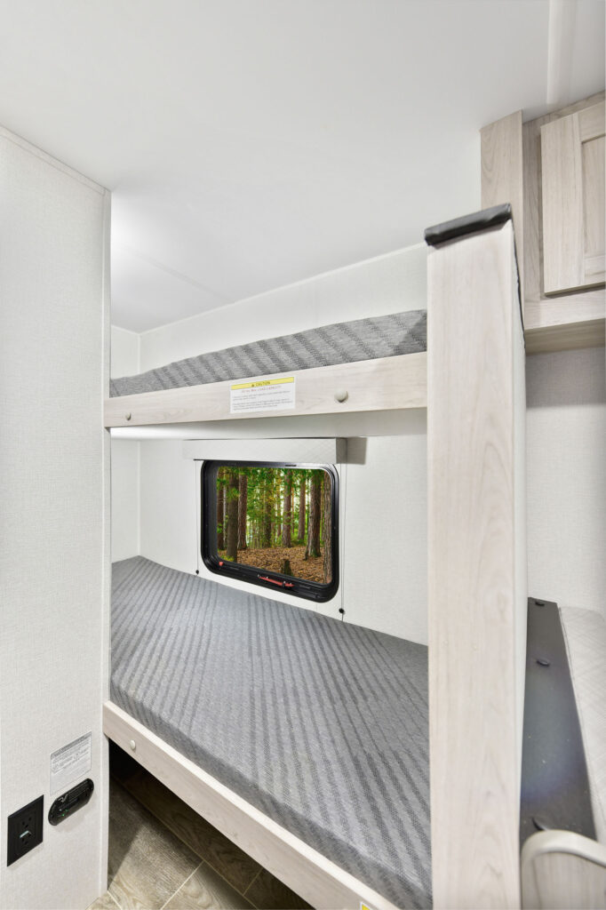 This image showcases the interior of the 2025 Prowler P17B travel trailer. The space is designed with a warm, inviting atmosphere, featuring comfortable seating and a compact dining area perfect for meals and relaxation. Light wood finishes and neutral upholstery add to the bright, spacious feel, while overhead cabinets provide ample storage for essentials. The layout is thoughtfully arranged to maximize functionality, making it an ideal space for family trips or weekend getaways.