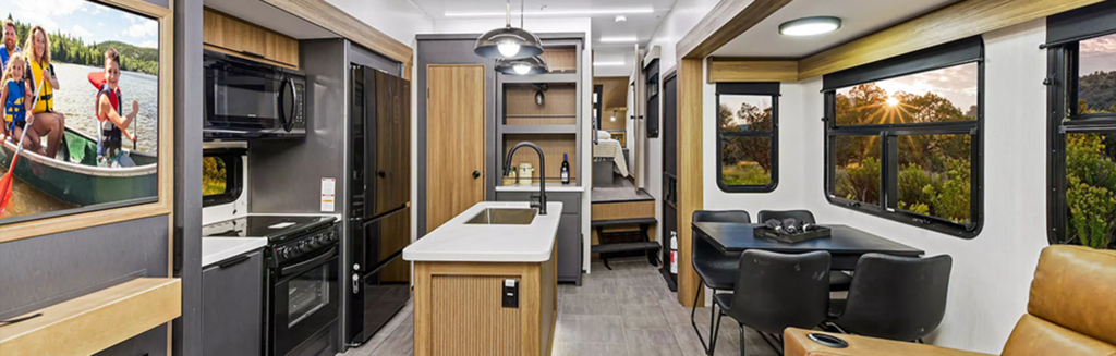 Inside a sleek 2025 RV, the kitchen and dining area offer panoramic windows framing a breathtaking sunset. Nearby, an inset reveals a group delighting in a lake boat ride, capturing the spirit of fifth wheels adventurous lifestyle.